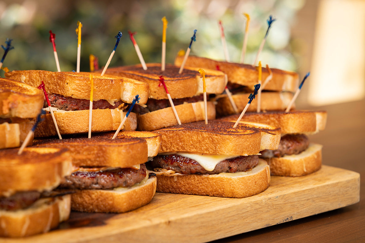 grilled patty melt on toasted bread with colorful toothpicks on wooden cutting board