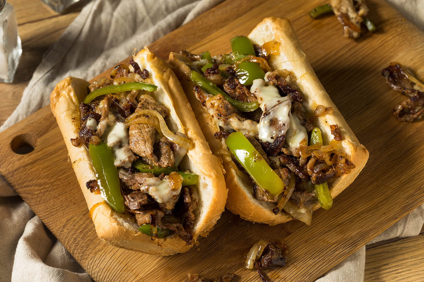 delicious looking Philly Cheese Sandwiches with green peppers on wooden cutting board
