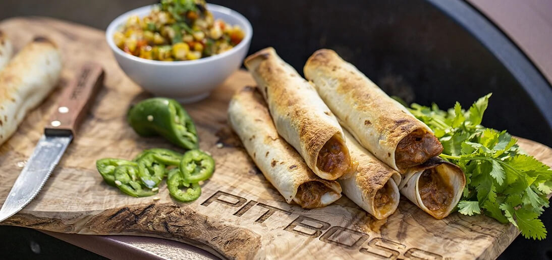 Homemade Pulled Pork Taquitos on wooden cutting board with jalapenos and cilantro