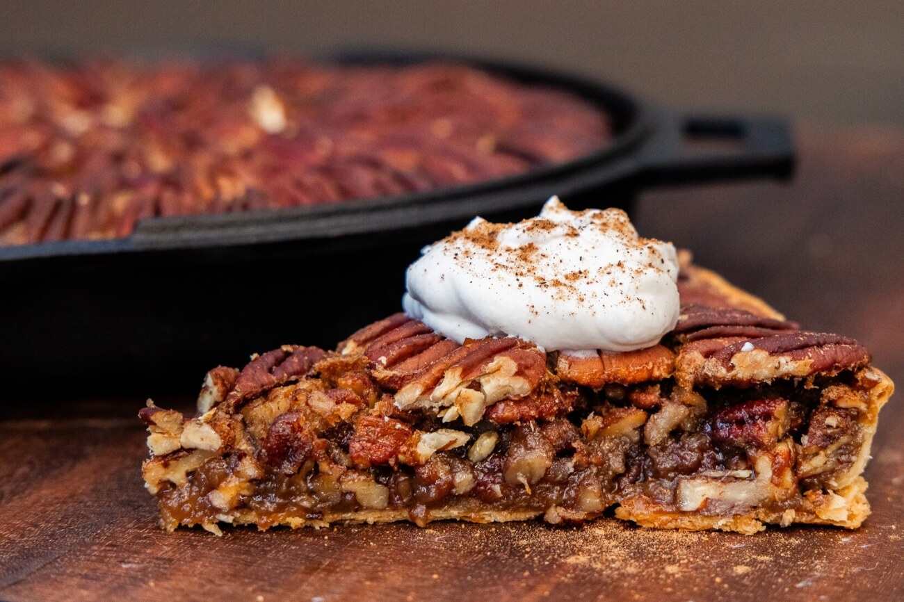 Warm and toasted smoked pecan pie cooked in a cast iron and baked on a buttery crispy crust with fresh maple whipped cream on top and a sprinkle of nutmeg