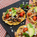 Colorful chicken tostadas with avocado, cherry tomatoes, cilantro, and crumbled cheese on a black tray.