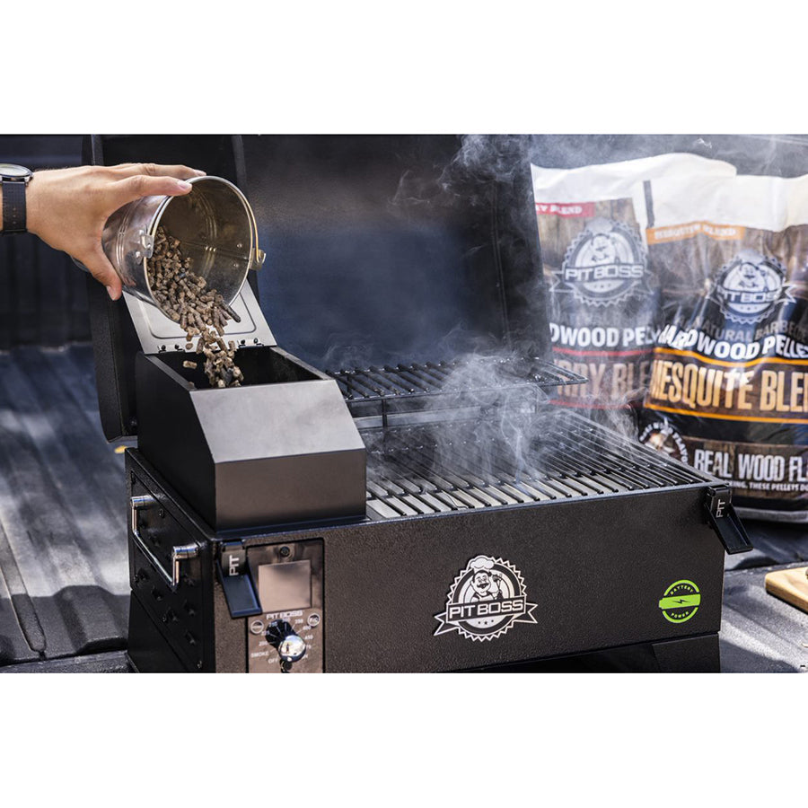 Pit Boss pellet grill with open lid, wood pellets being poured in, digital control panel, and smoking grill grates.