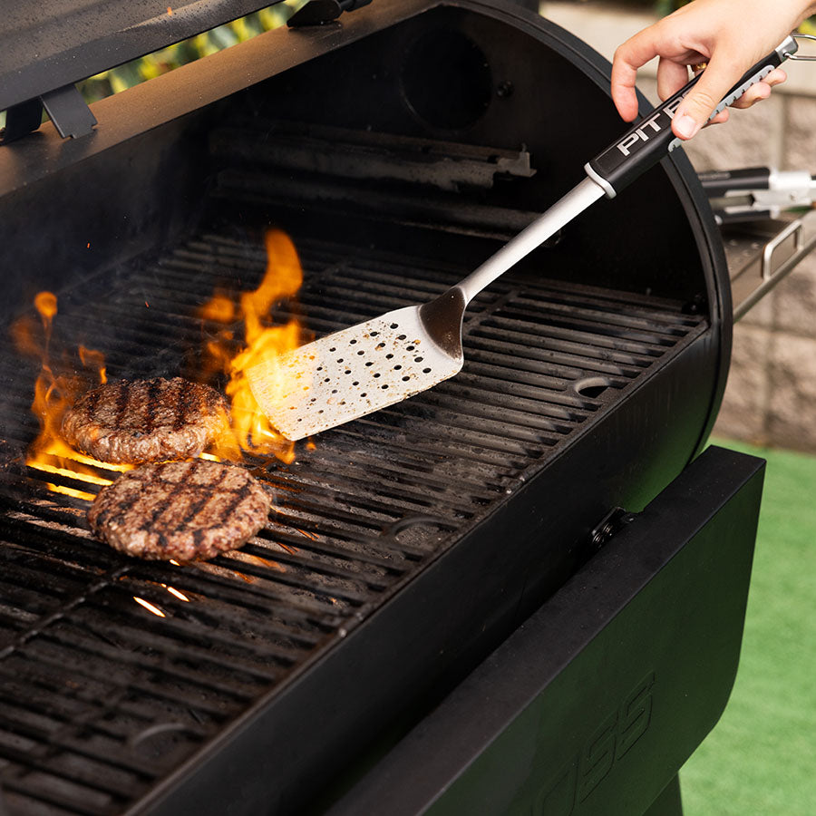 Black Pit Boss grill with spatula flipping burgers over flame.