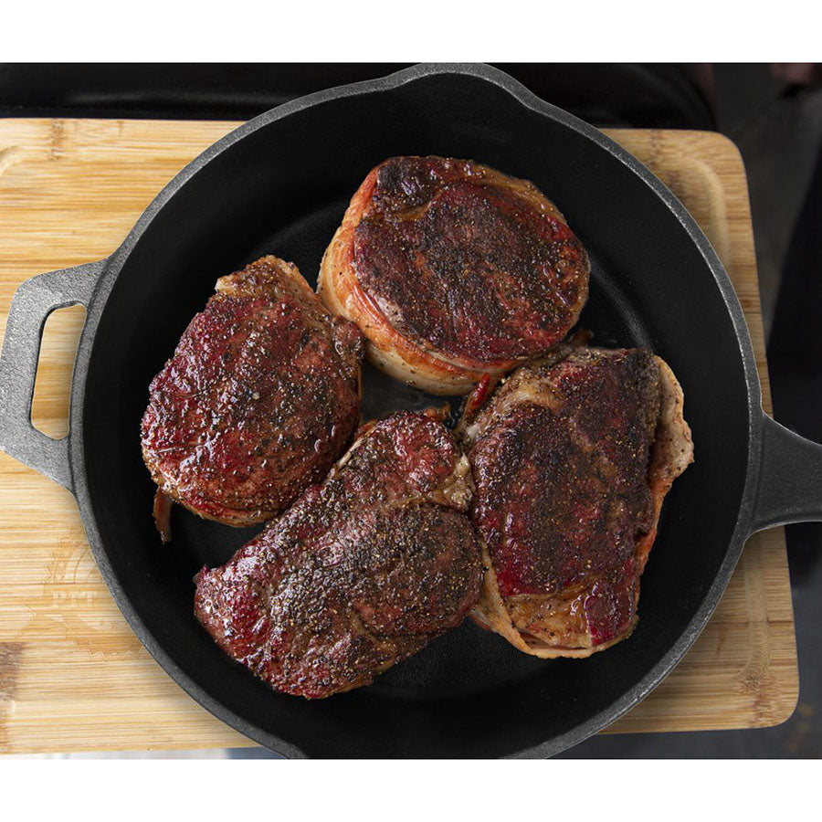 Black cast iron skillet with four bacon-wrapped steaks.