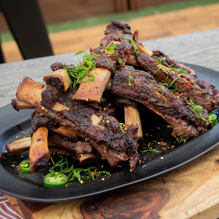 "Glazed beef ribs with green garnish on black plate."