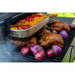 Grill with whole chickens, red onions, and a tray of baked macaroni topped with red peppers. Outdoor cooking scene.