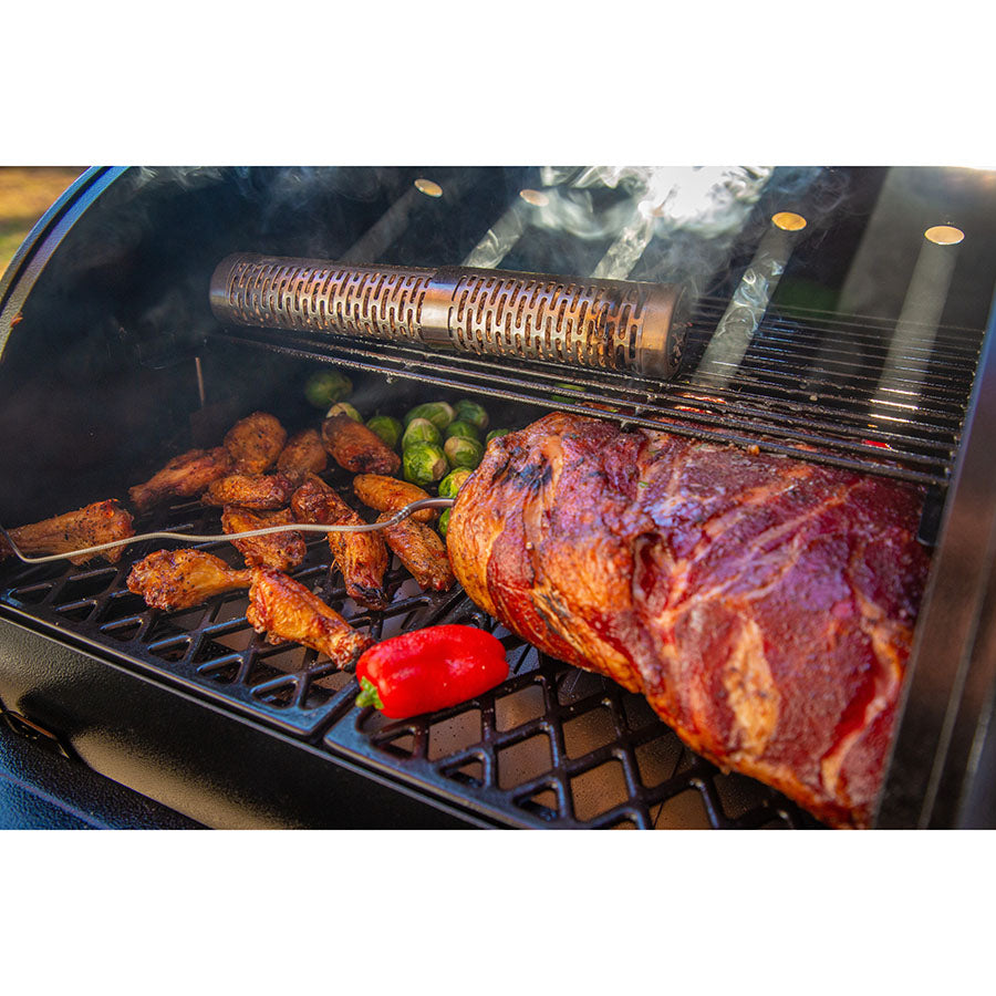 Smoker tube on a grill with smoked meat, chicken wings, Brussels sprouts, and a red pepper. Stainless steel, vented design.