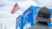 Black PITBOSS trucker hat worn by person near blue racing trailer.