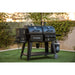 Black Pit Boss Competition Series dual smoker grill with wheels and side shelves.