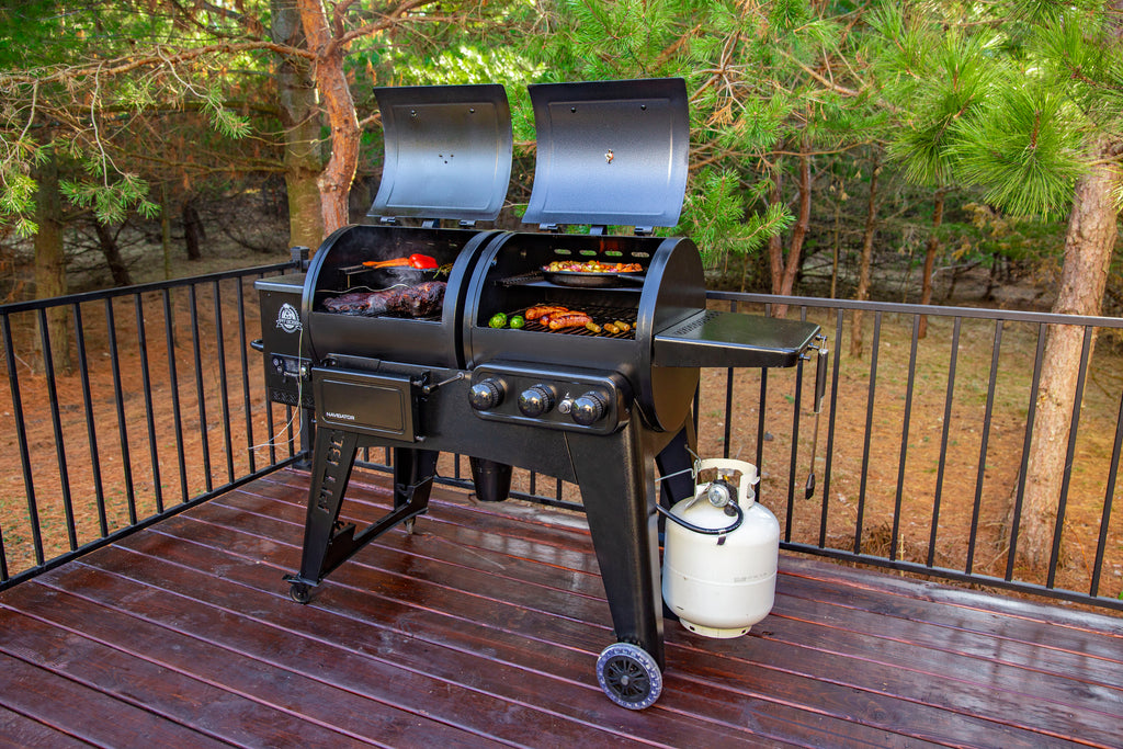 Black dual-burner gas grill with side burner and propane tank, set on wooden deck.