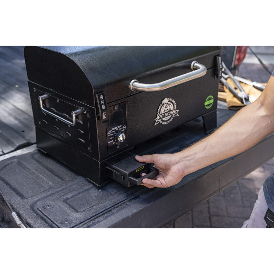 Portable black Pit Boss grill with a handle, battery compartment, and control panel, shown on a truck bed.