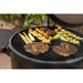 Black round charcoal grill with steaks, vegetables, and burgers cooking.