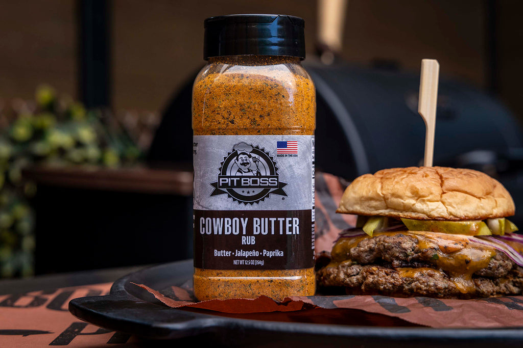 Orange Pit Boss Cowboy Butter Rub spice blend bottle with barbecue background.