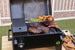 Black electric grill with digital control, grilling steaks, sausages, chicken wings, and asparagus. Open lid, outdoor sett...