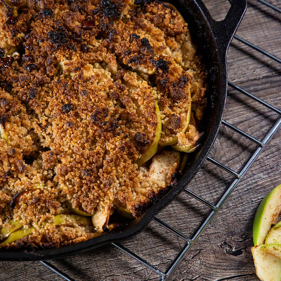 Apple crumble in black cast iron skillet on cooling rack.