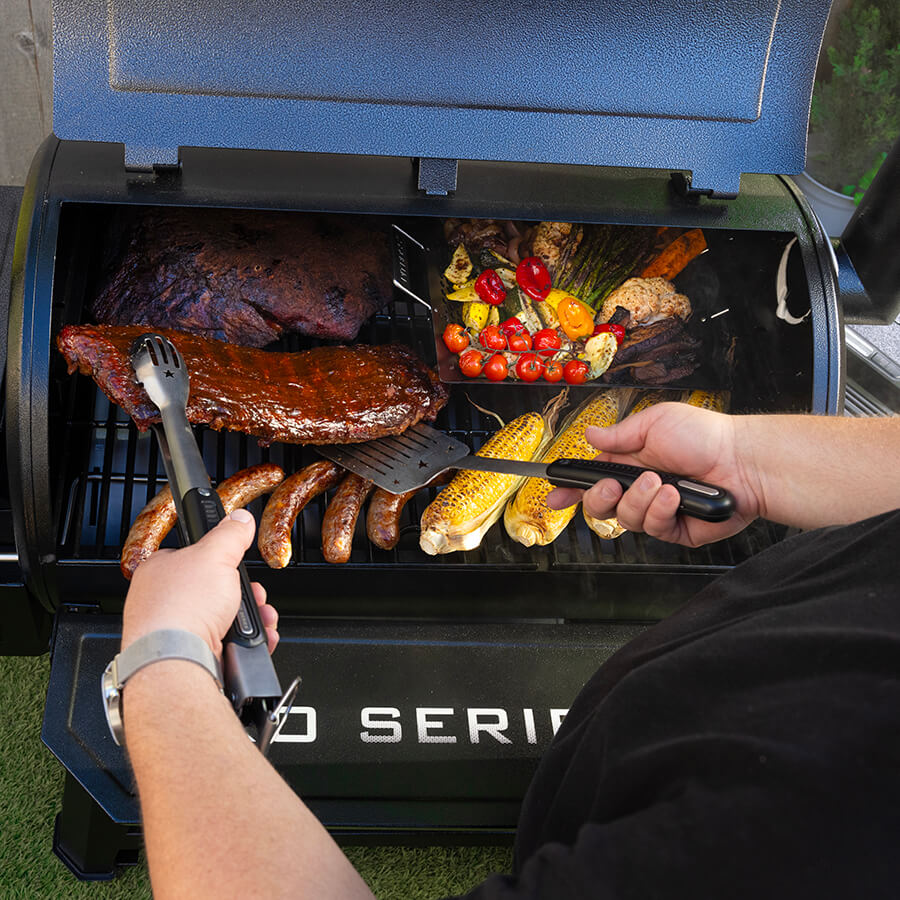 Blue BBQ grill with meats, sausages, corn, and vegetables cooking.