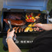 Blue BBQ grill with meats, sausages, corn, and vegetables cooking.