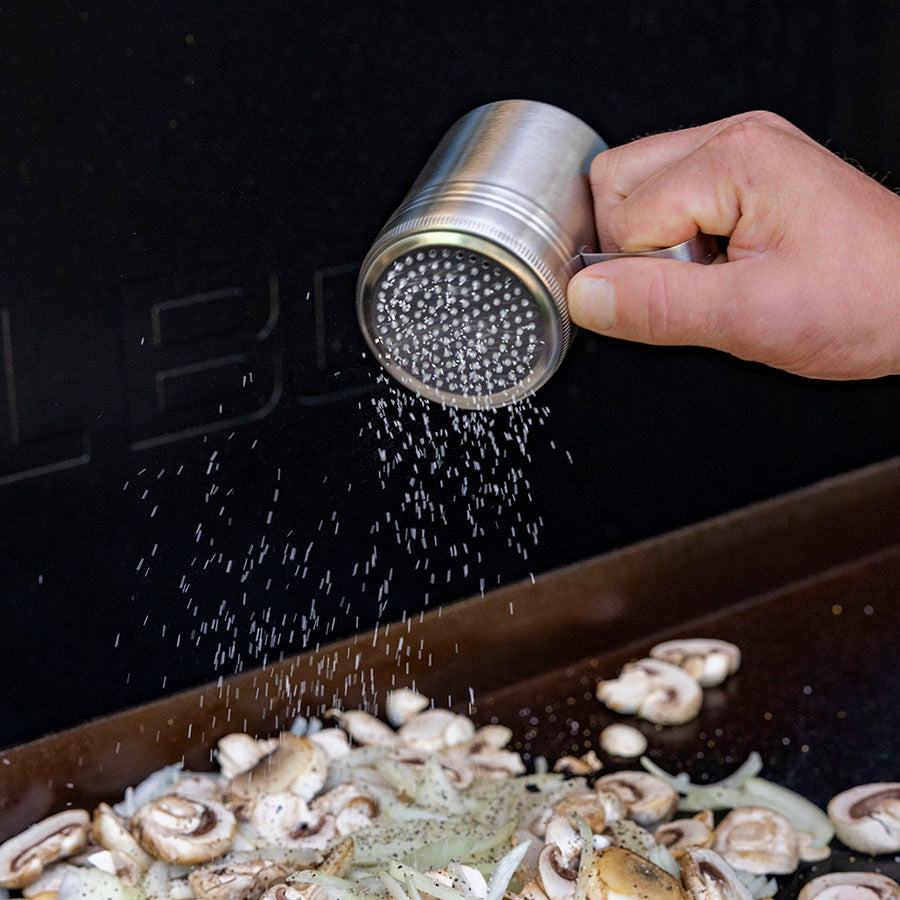 Silver pepper grinder sprinkling pepper onto mushrooms.
