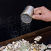 Silver pepper grinder sprinkling pepper onto mushrooms.