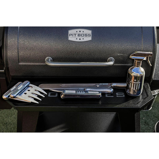 Black Pit Boss grill with accessories: fork, knife, and spray bottle.