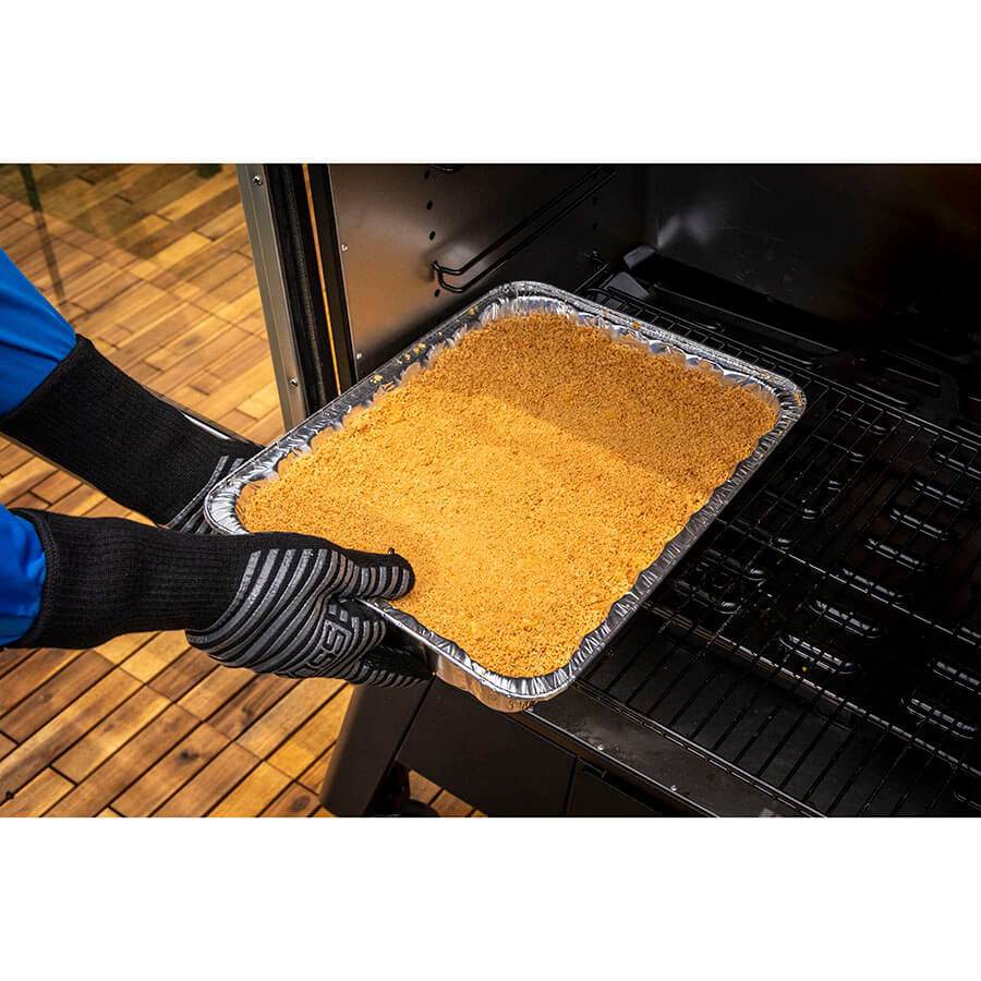 Aluminum tray with yellow food being placed in oven by gloved hands.