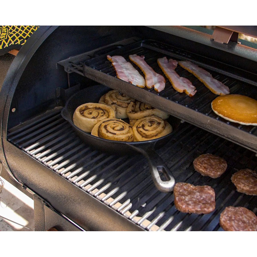 Black grill with cast iron skillet, bacon, cinnamon rolls, and breakfast patties.