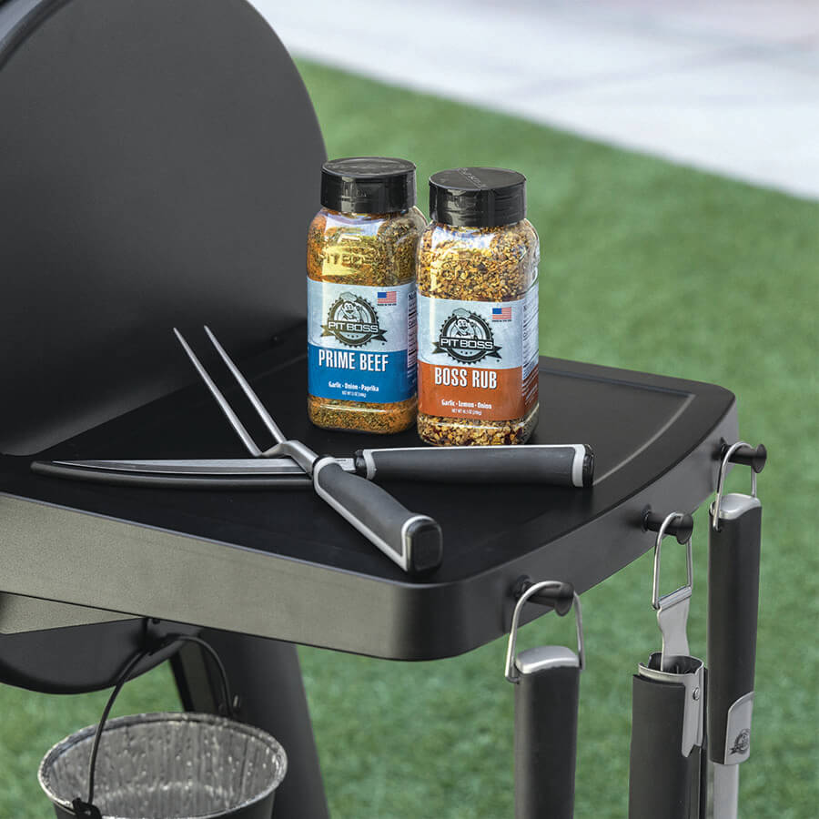 Black Pit Boss grill with seasoning bottles and tongs.