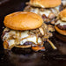 Golden burger with melted cheese, mushrooms, and onions on a black surface.