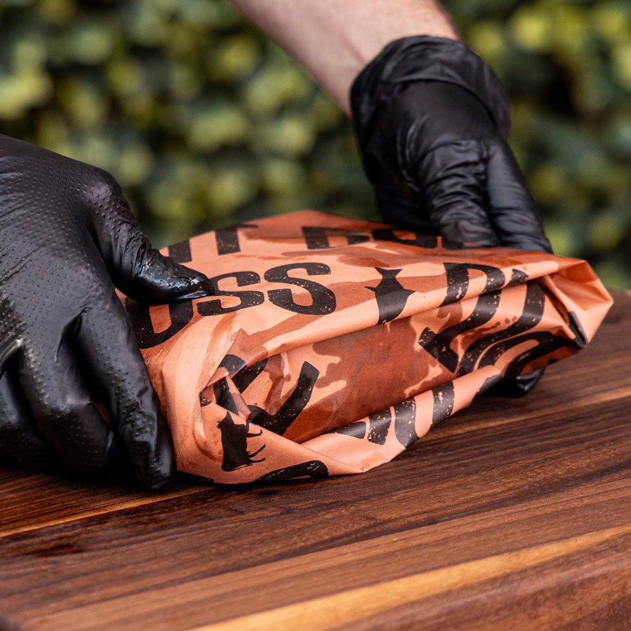 Brown camouflage-patterned fabric with black text, held by hands wearing black gloves.
