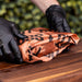 Brown camouflage-patterned fabric with black text, held by hands wearing black gloves.