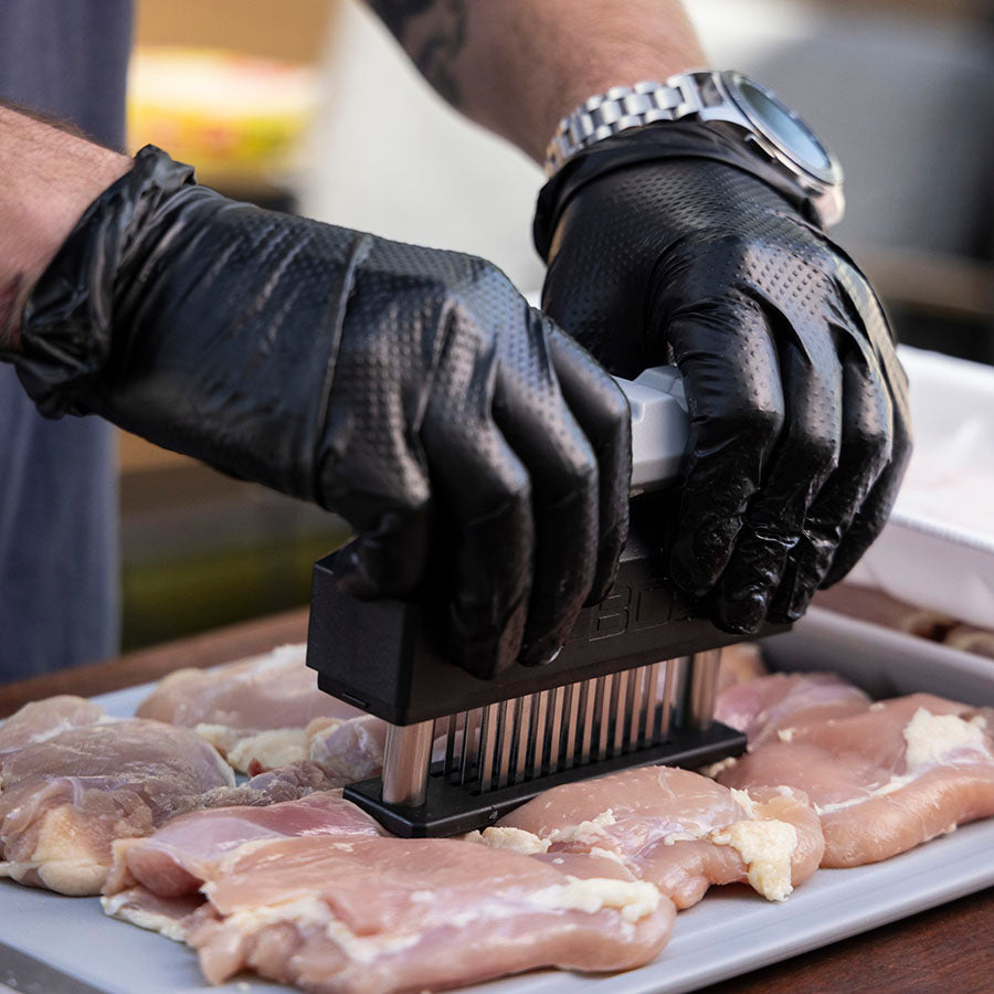 Black meat tenderizer tool being used on raw chicken.