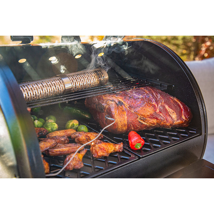Smoker tube in grill with smoking meat, chicken wings, peppers, and Brussels sprouts. Stainless steel, smoke visible.
