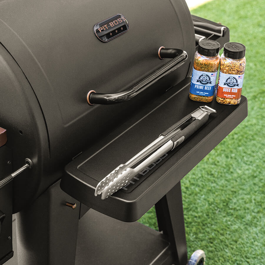 Black Pit Boss grill with seasoning bottles and tongs on side shelf.