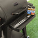 Black Pit Boss grill with seasoning bottles and tongs on side shelf.