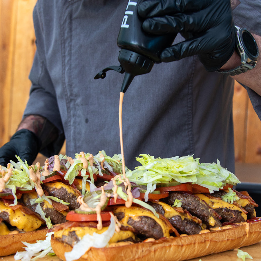 Cheeseburger with lettuce, tomato, bacon, and sauce being drizzled.