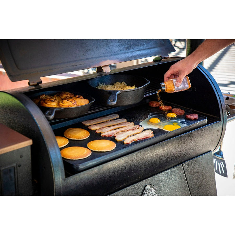 Black outdoor grill with griddle, cooking pancakes, bacon, eggs, and skillet dishes.