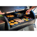 Black outdoor grill with griddle, cooking pancakes, bacon, eggs, and skillet dishes.
