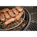 Grill with several steaks cooking over open flames on a round metal grate, surrounded by a patterned metal edge.