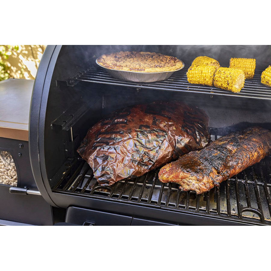 Black grill with smoking meats, corn, and pie.