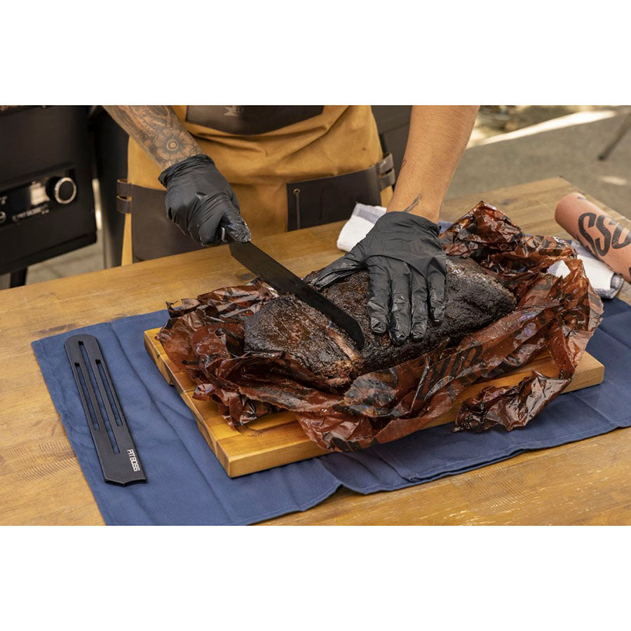 Black-handled knife slicing smoked brisket on wooden cutting board.
