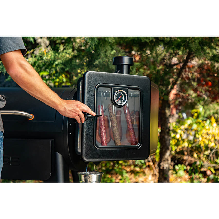 Black electric smoker with glass window showing sausages inside, thermometer visible.