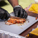 Black gloves cutting seasoned chicken on a white cutting board.